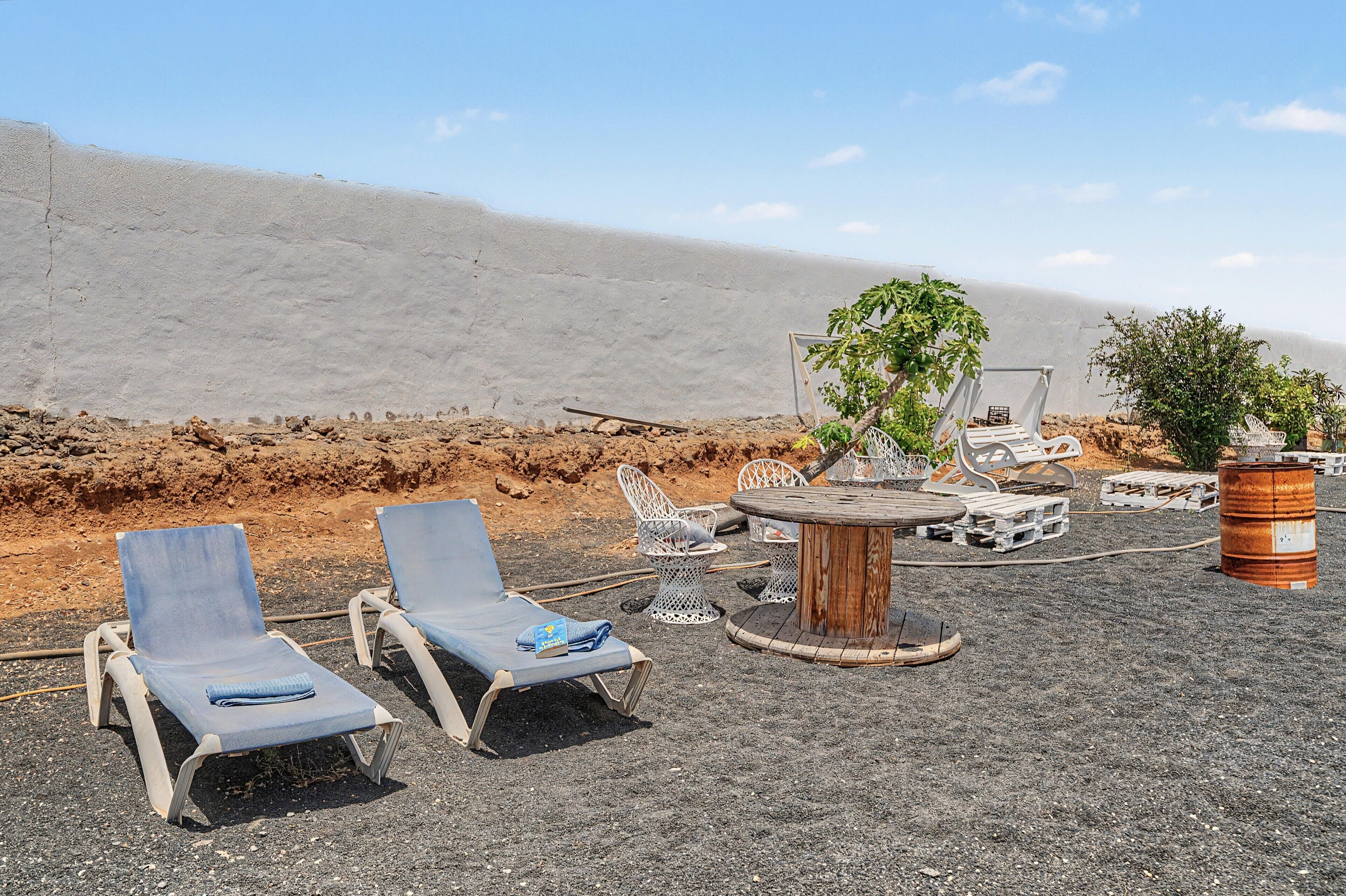 Uma área de estar à beira-mar com espreguiçadeiras, uma mesa redonda de madeira e plantas em vasos.