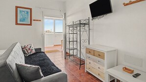Un salon comprenant un canapé, un téléviseur fixé au mur, un meuble en bois et un étendoir à linge en métal.