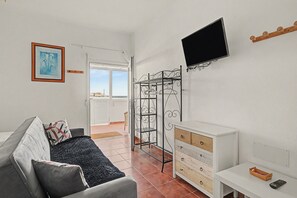 Een woonkamer met een bank, een aan de muur bevestigde televisie, een houten kast en een metalen droogrek.