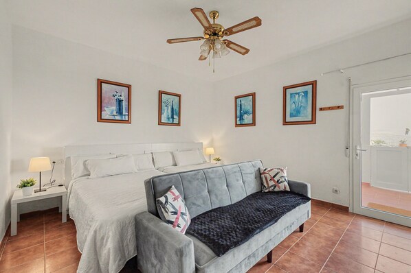A bedroom with a bed, a sofa, a nightstand with a lamp, and wall-mounted artwork.