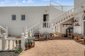 A courtyard with a white building, a staircase, wicker furniture, and potted plants.