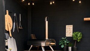 Eine moderne Außenküche mit eingebautem Grill, Schneidebrett aus Holz und hängendem Kochgeschirr.