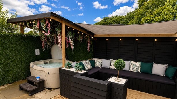 Ein Whirlpool, eine Sitzecke und eine Pergola mit Lichterketten in einem Garten.