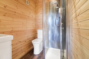 Une salle de bain rustique, avec une cabine en bois, une douche vitrée, des toilettes blanches et un lavabo blanc.