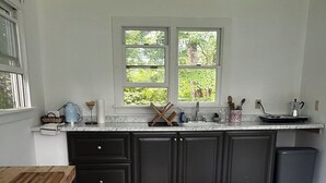 A kitchen with dark cabinets, a marble countertop, a window with a view of greenery, and a striped rug. - Cape Rosier Cozy Guesthouse (Harborside)