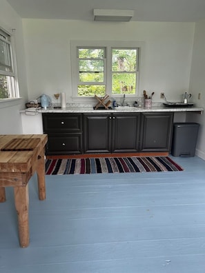 A kitchen with dark cabinets, a marble countertop, a window with a view of greenery, and a striped rug.