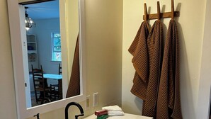 A bathroom with a white sink, a mirror, a towel rack with towels, and a view into a dining area. - Cape Rosier Cozy Guesthouse (Harborside)