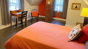 Un dormitorio con cama, escritorio, silla y un pilar de ladrillo.