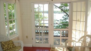 A room with a white wicker sofa, a small table, and a view of a body of water through a glass door. - Hearthstone Cottage , Private cottage on Waters Edge! (Blue Hill)