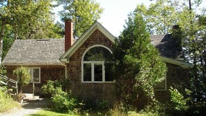 A stone house with a chimney, a front door, and a large arched window. - Hearthstone Cottage , Private cottage on Waters Edge! (Blue Hill)