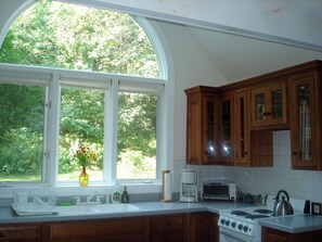Una cocina con un ventanal grande, armarios de madera, una estufa y una cafetera.