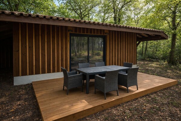 A wooden cabin with a deck, a table, and chairs. - Les cabanes (Noaillan)