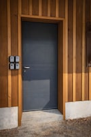 Entrada de um edifício moderno com porta escura, painéis de madeira e um degrau de concreto.