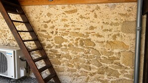 A ladder leaning against a stone wall with an air conditioning unit below it. - Les cabanes (Noaillan)