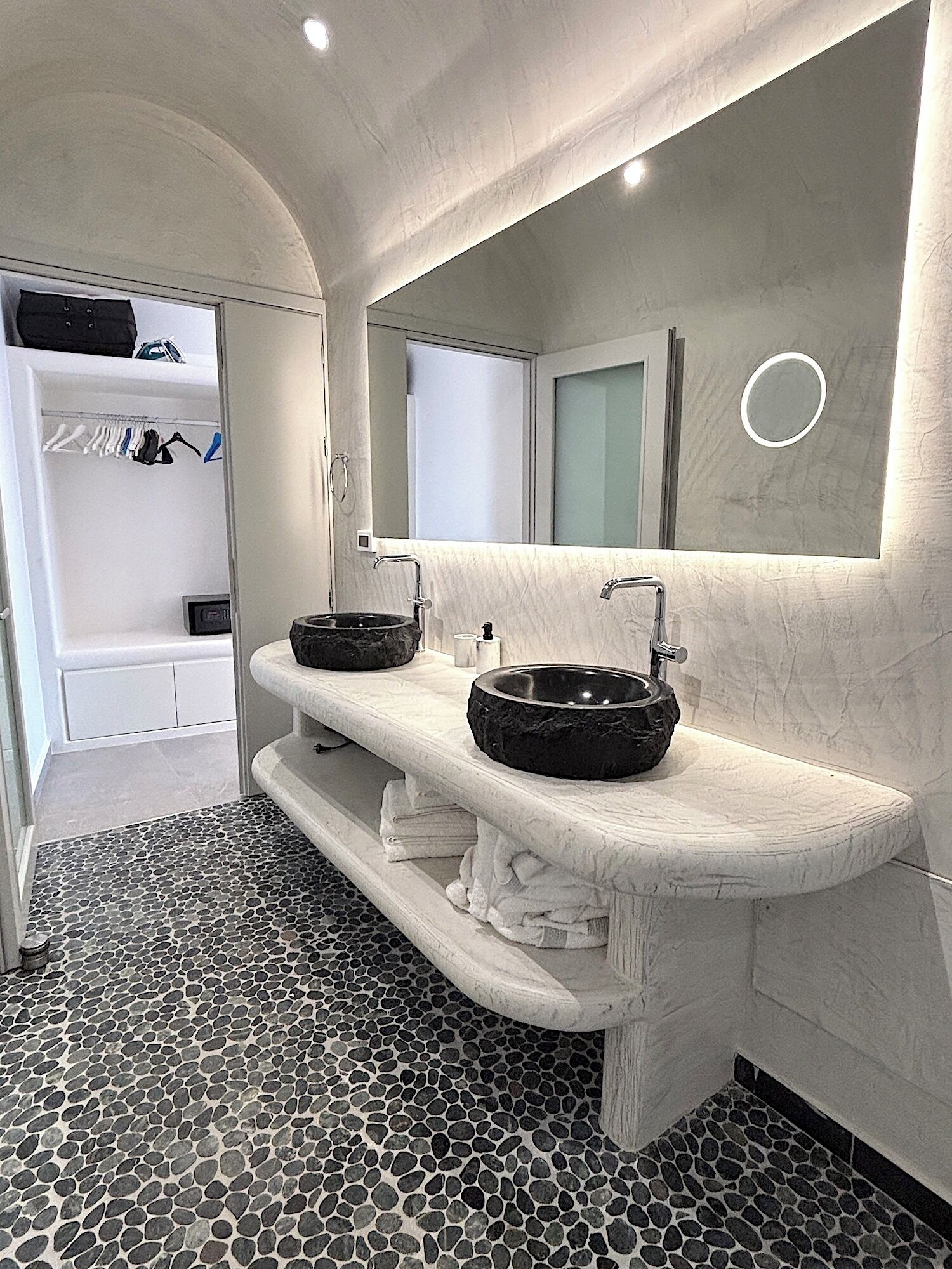 A modern bathroom with a marble vanity, a round mirror, and a built-in shower.