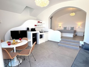 A compact, modern room with a dining area, kitchenette, and a bed with a staircase leading to a balcony. - Villa Helionira (Santorin)