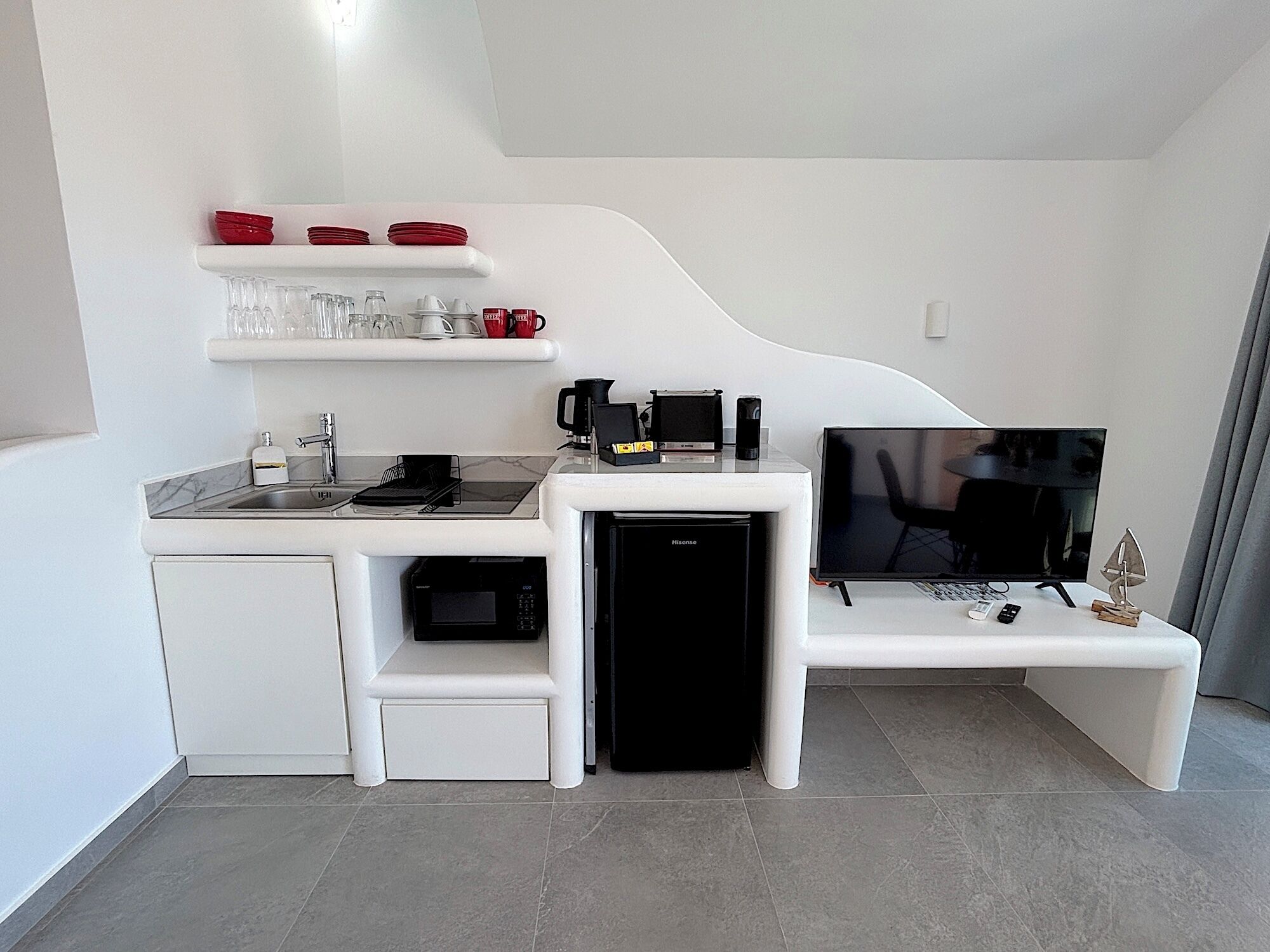 Una kitchenette compacta con microondas, cafetera y televisión de pantalla plana.