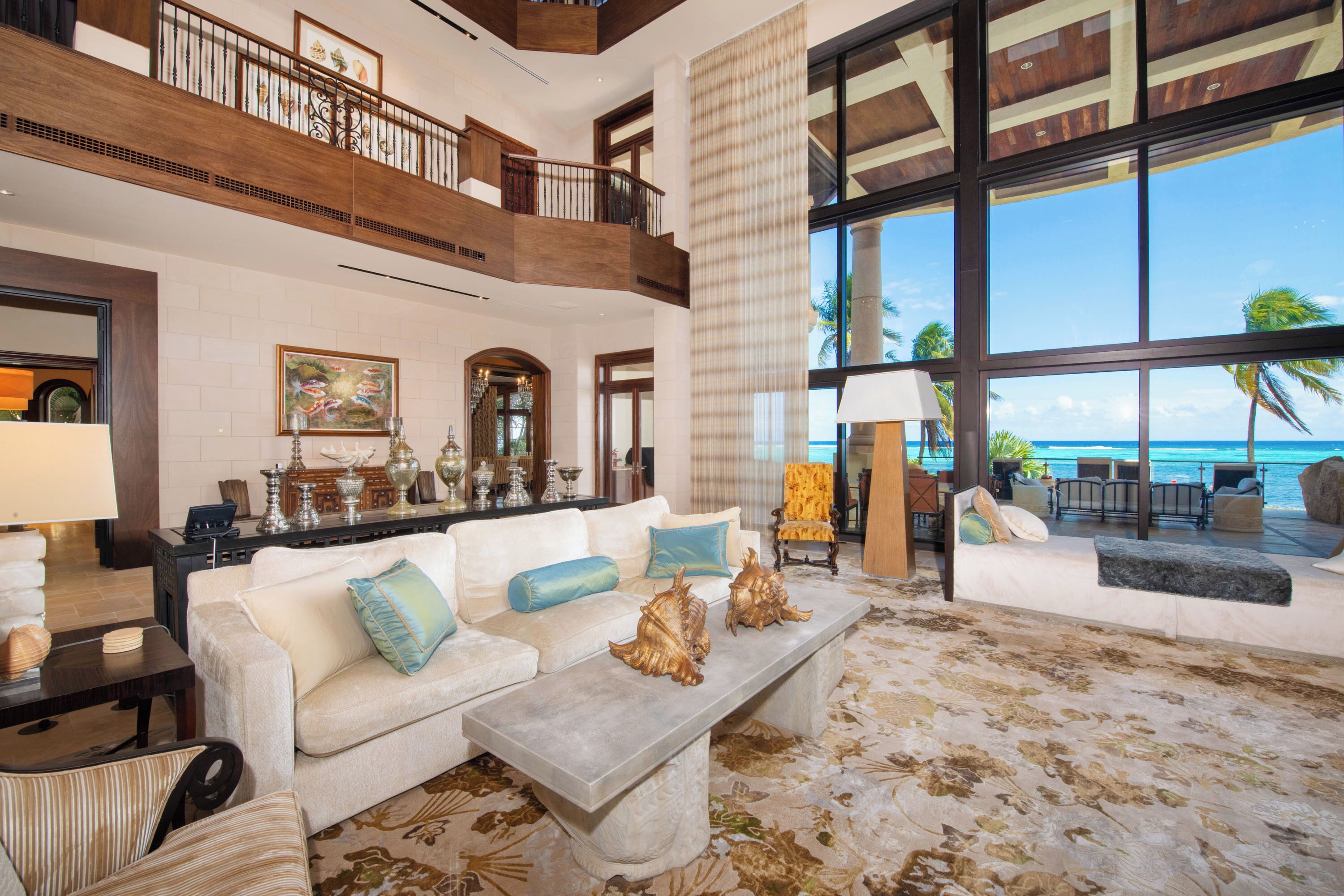A spacious living area with a high ceiling, a balcony overlooking the ocean, and a large window providing a view of the sea.