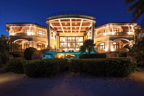 A large, luxurious hotel with a central courtyard, multiple balconies, and a swimming pool. - Castillo Caribe: Ultra-Luxe Estate w/Pool Grotto, Tennis & Pickle Ball Courts + Home Spa & Gym (South Sound)