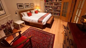 Quarto com cama grande, mesas de cabeceira, estante, escrivaninha e uma cadeira.