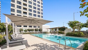 Une piscine avec des chaises longues, un espace de repos couvert et un bâtiment moderne en arrière-plan.