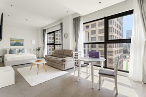 A modern living room with a sofa, a dining table, and a view of the city through large windows. - Silkhaus Comfy Studio Stay in Pixel Tower Al Reem Island (Abu Dhabi)
