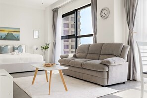 A modern living room with a sofa, a small table, a bed, and a large window with curtains. - Silkhaus Comfy Studio Stay in Pixel Tower Al Reem Island (Abu Dhabi)