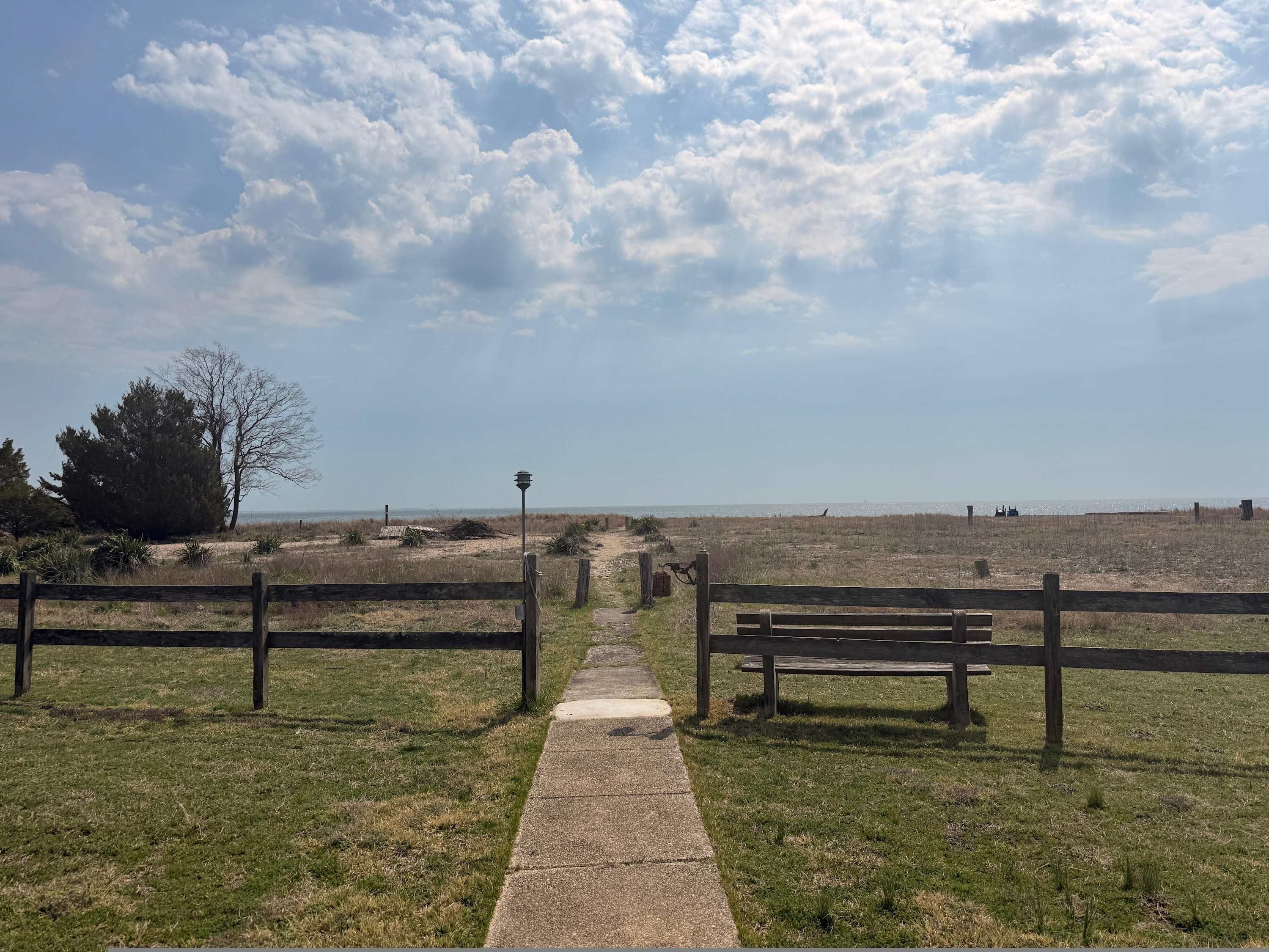 A pathway leading to a beach with wooden fences and benches.