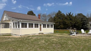 Een gelijkvloers huis met een overdekte veranda, schoorsteen en gazon.