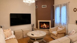 Uma sala de estar com lareira, televisão e um candelabro.