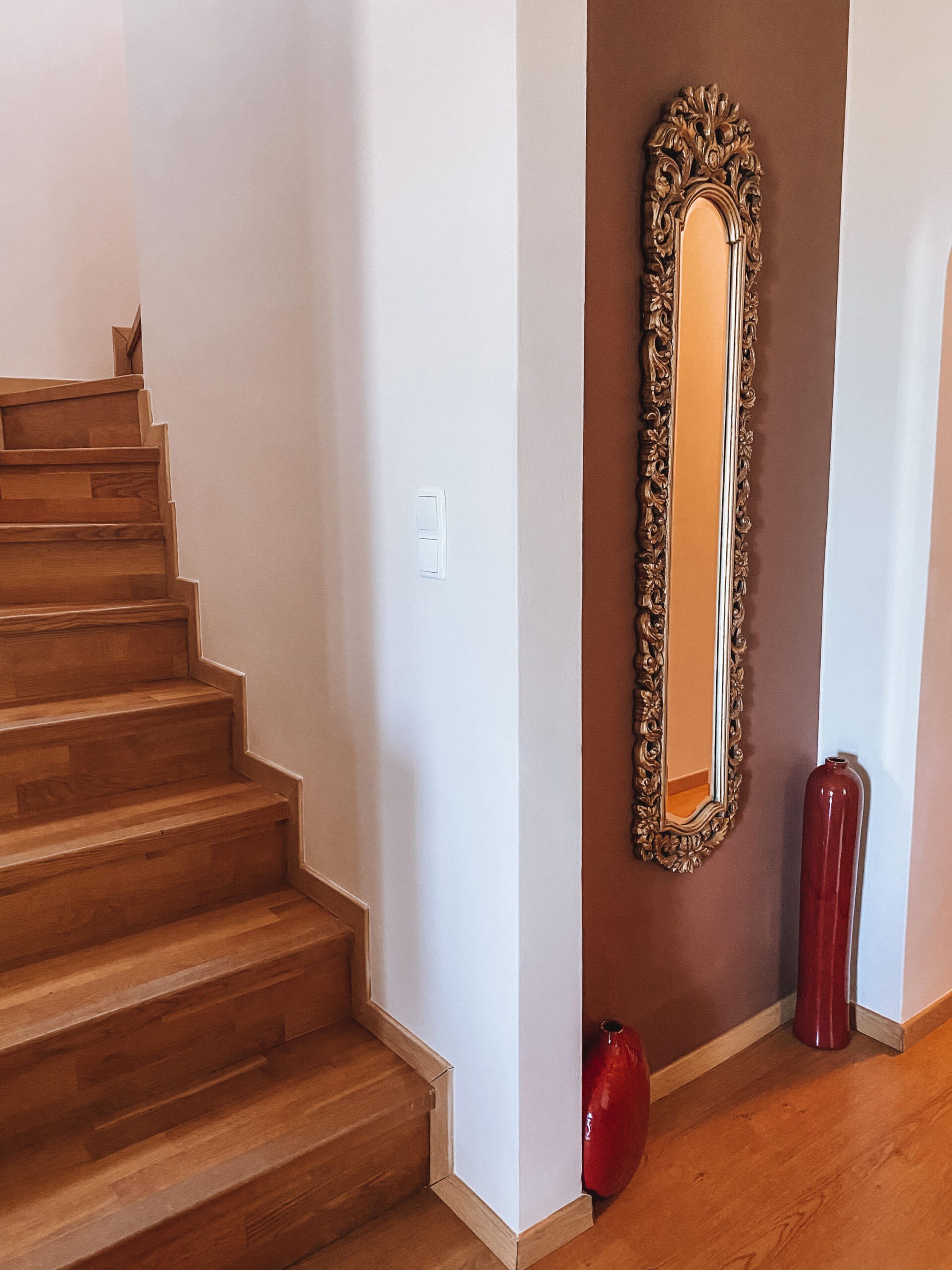 Eine Treppe mit Holzbodenstufen, ein an der Wand befestigter Spiegel und ein roter Vasen.
