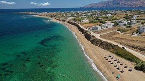 Vista aérea de uma área costeira com águas turquesa cristalinas, uma praia de areia e uma zona residencial com edifícios brancos.
