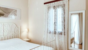 Quarto com cama, abajur, janela com cortinas e um espelho.