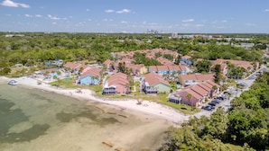 An aerial view of a coastal resort with beachfront villas, a marina, and a city skyline in the background. - Your own Tropical Resort Heated Pool Pickleball (St. Petersburg)