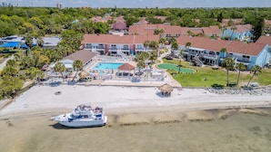 An aerial view of a resort with a swimming pool, beach, and a boat docked near the shore. - Your own Tropical Resort Heated Pool Pickleball (St. Petersburg)