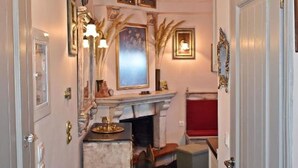 Un pasillo con candelabro, obras de arte enmarcadas, chimenea y un banco rojo.
