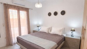 A bedroom with a bed, two bedside tables with lamps, a window with curtains, and wall decorations. - Villa Therme Athen-sea View Jacuzzi Santorini Stay (Santorini)
