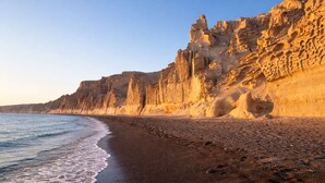 A beach with a rocky cliff, a sandy shore, and a clear sky. - Villa Therme Athen-sea View Jacuzzi Santorini Stay (Santorini)