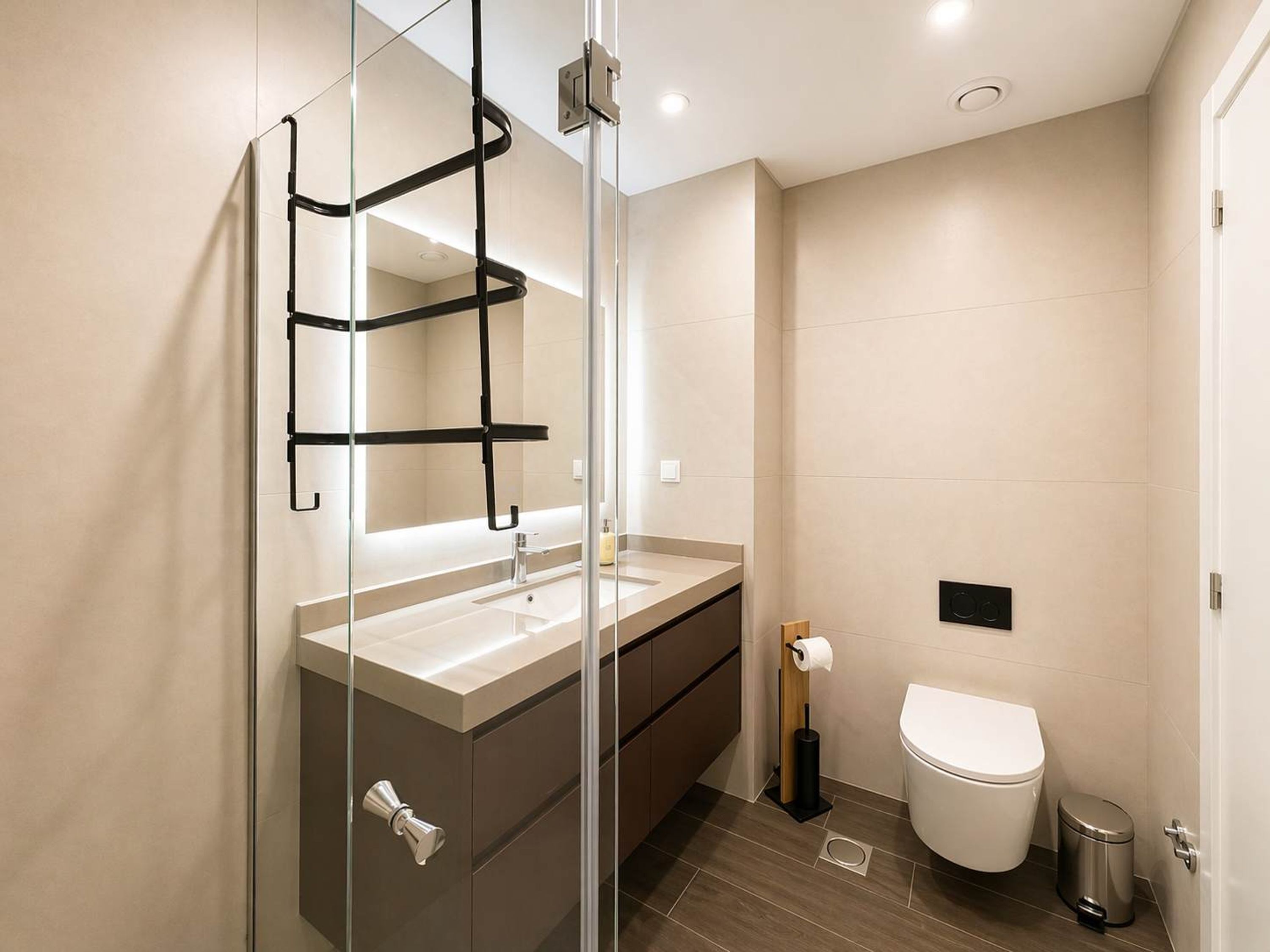 Une salle de bain moderne avec une douche à parois de verre, un lavabo avec un miroir, des toilettes et une poubelle.