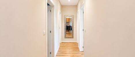 Un couloir doté d’un plancher en bois, de murs blancs et de portes donnant accès aux pièces.
