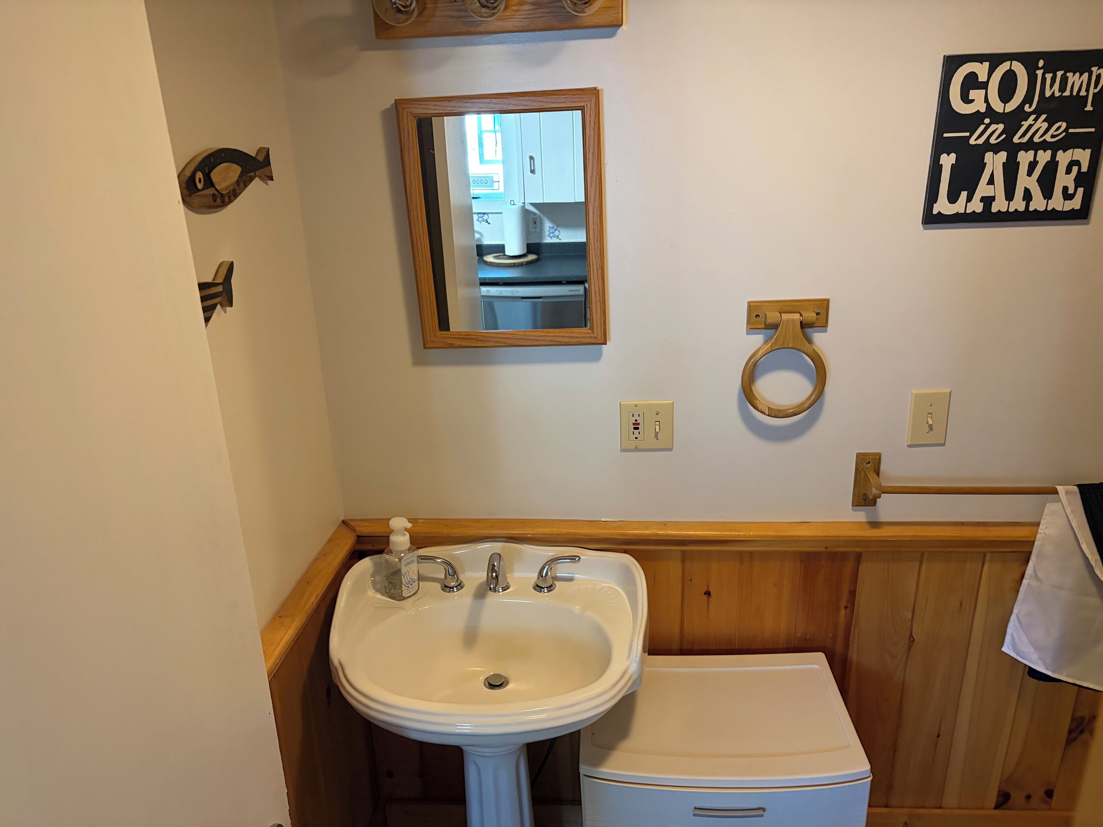 Een badkamer met een wastafel, spiegel, houten decoratie aan de muur en een bordje met de tekst 'GO jump in the LAKE'.