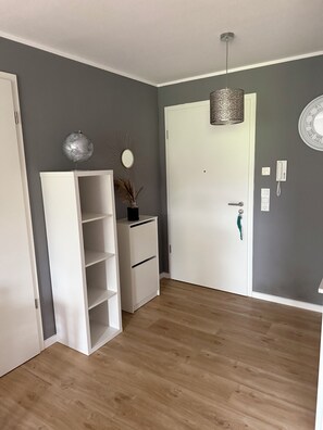 Ein Zimmer mit einem weißen Wandschrank, einer weißen Regaleinheit, einer Hängeleuchte, einer Tür mit grünem Griff und einem an der Wand befestigten Telefon.