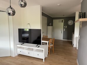 A modern living room with a flat-screen TV, wooden dining table, and chairs.