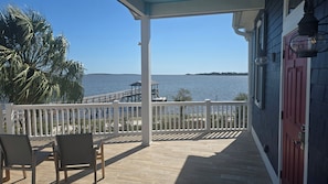 A covered deck with wooden flooring, white railings, and two chairs. - Windswept Cottage - private pier and beach access (Cedar Key)