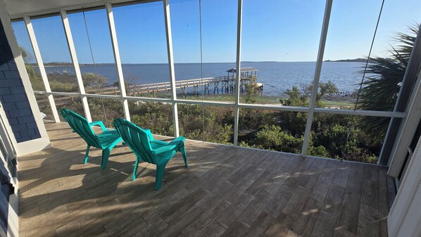 A balcony with wooden flooring and two turquoise chairs, overlooking a body of water with a pier and vegetation. - Windswept Cottage - private pier and beach access (Cedar Key)