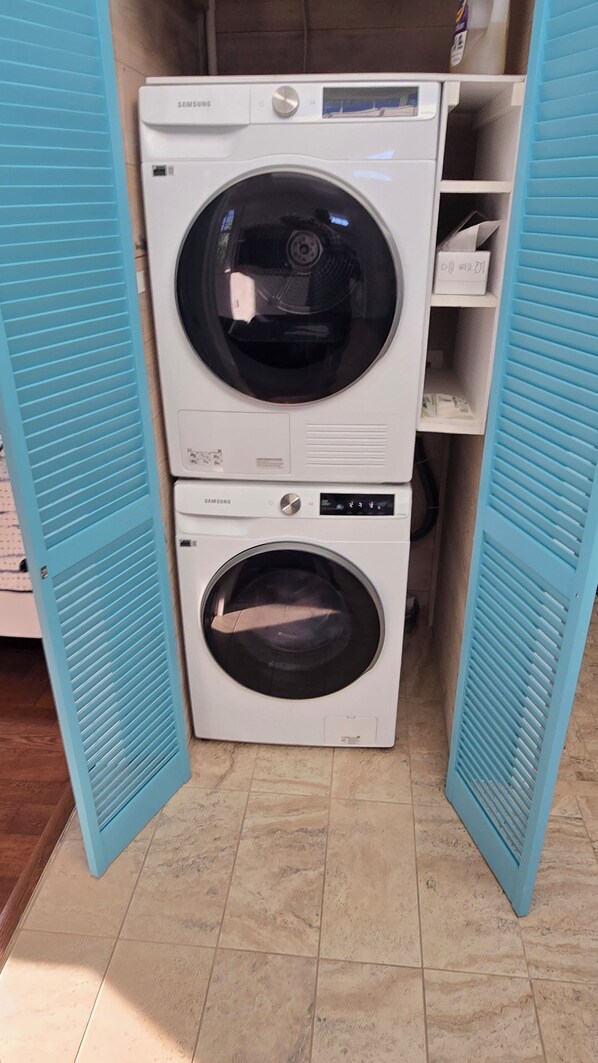 A laundry room with two stacked Samsung washing machines and a blue door. - Windswept Cottage - private pier and beach access (Cedar Key)