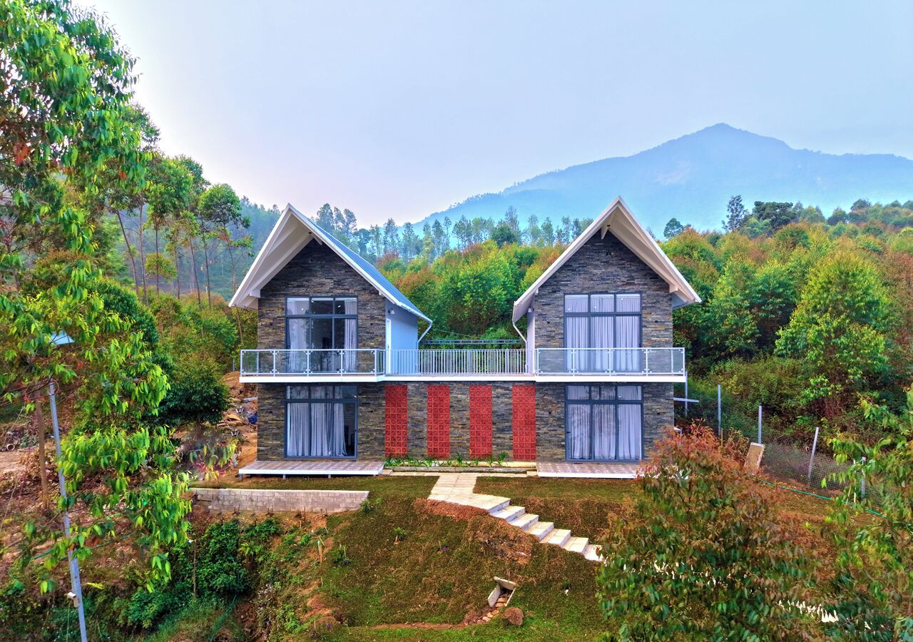 A modern two-story house with a stone facade, a balcony, and a view of a mountainous landscape.