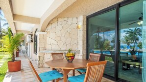 Une terrasse avec une table et des chaises, un mur en pierre et une vue sur la piscine et l’océan.