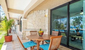 Eine Terrasse mit Tisch und Stühlen, eine Steinmauer und Blick auf Pool und Meer.
