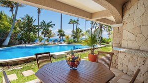 Un espace aménagé au bord de la piscine, avec une table, des chaises et un panier de fruits.